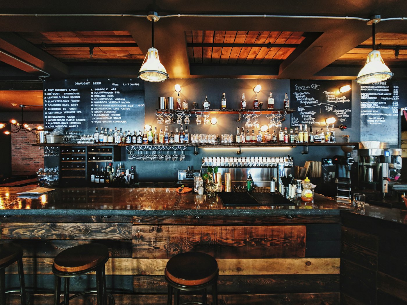 A reclaimed-timber pub bar with a chalkboard draught list, rows of taps and warm pendant lights — placeholder photo, not the Axe & Anchor’s bar