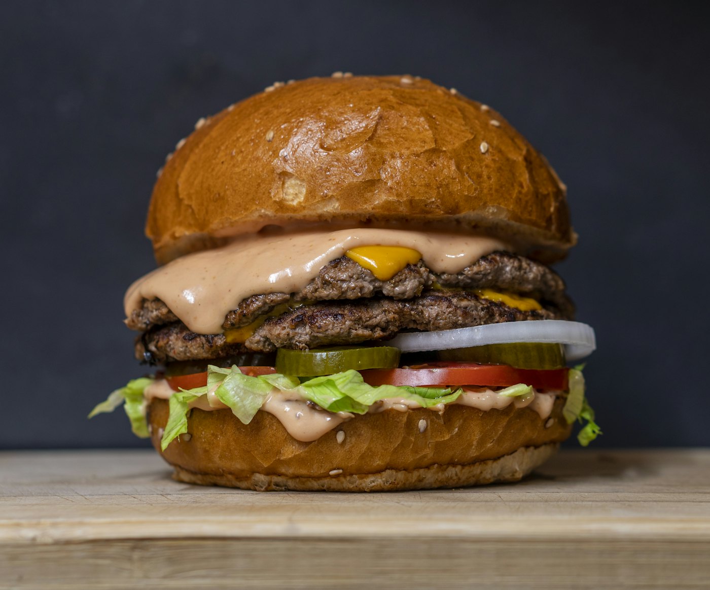 A tall double cheeseburger on a toasted bun over dark wood — placeholder photo, not the Axe & Anchor’s kitchen