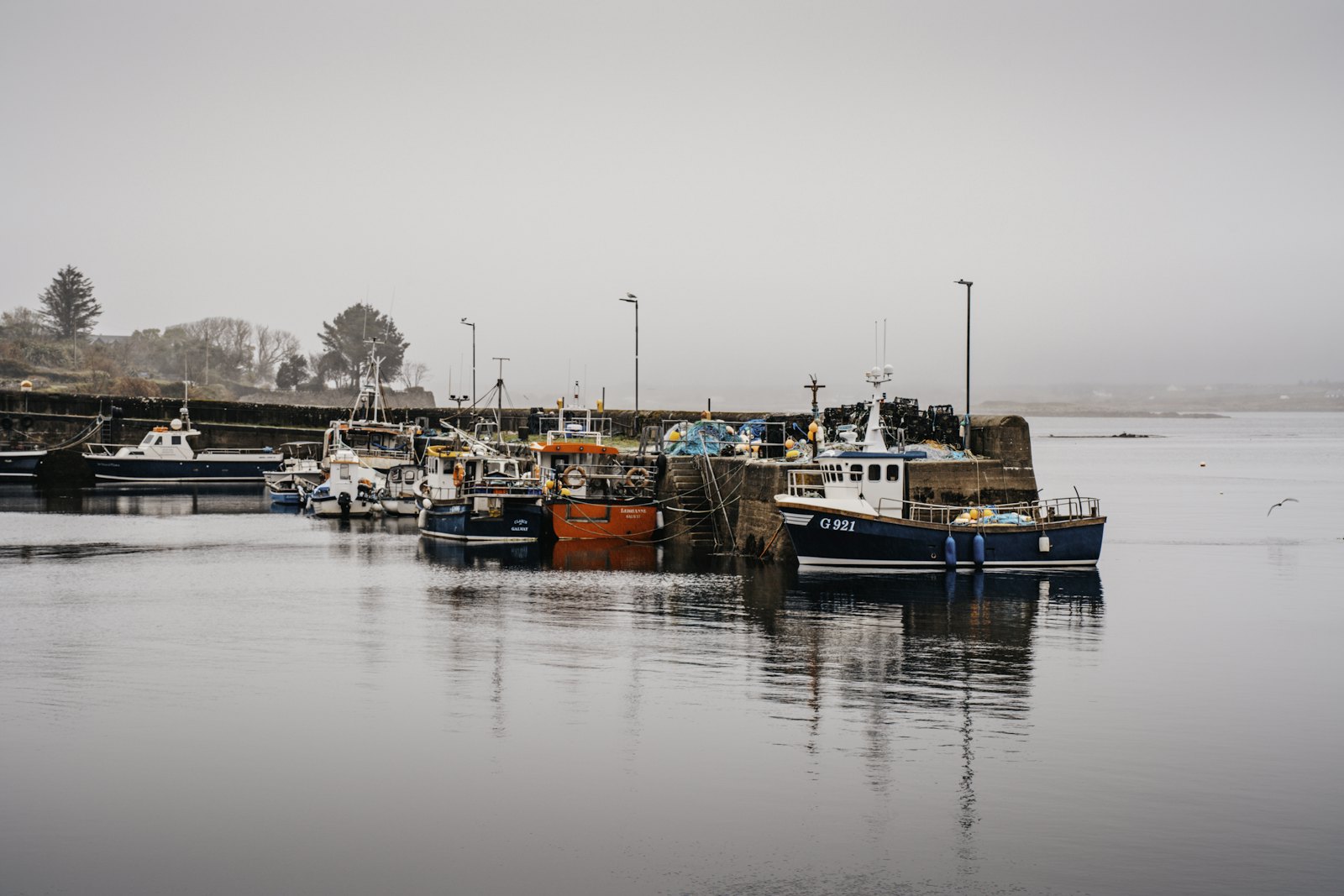 Fishing boats moored along a quiet, misty northern harbour with a low forested shore — placeholder photo standing in for the Axe & Anchor’s waterfront